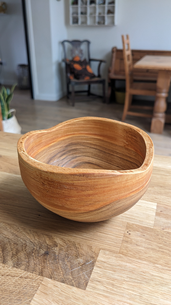 A small, turned, cherry wood bowl where the rim has been left to show the natural contours of the tree